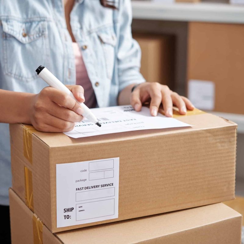 Close-up of woman writing address on parcel for sending